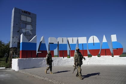 Soldados rusos pasan junto a un nombre de la ciudad repintado con los colores de la bandera rusa en la entrada de Mariupol, en el territorio que está bajo el control del Gobierno de la República Popular de Donetsk, en el este de Ucrania, el domingo 12 de junio de 2022.