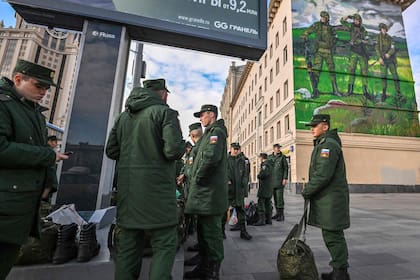 Soldados rusos recientemente reclutados esperan su salida mientras se encuentran cerca de un mural que representa a militares rusos con brazaletes con el símbolo "Z", cerca de la terminal ferroviaria de Paveletsky, en el centro de Moscú el 16 de octubre de 2022.