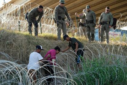 Soldados y guardias de Texas ayudan a una migrante que quedó atrapada en un alambre de púas después de cruzar el Río Grande desde México hacia EEUU, el 1 de agosto de 2023, en Eagle Pass, Texas (Archivo)
