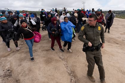 Solicitantes de asilo caminan tras un agente de la Patrulla Fronteriza hacia una camioneta para ser procesados tras cruzar la frontera con México, el jueves 25 de abril de 2024. (AP Foto/Gregory Bull)