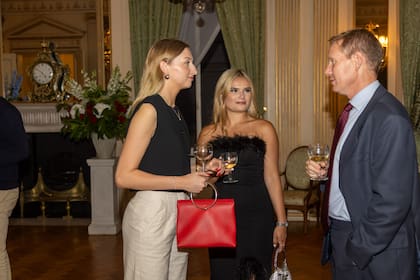 Sophie White, Phoebe Leake y el teniente coronel Tom Armitage charlan durante el cóctel celebrado en la embajada.