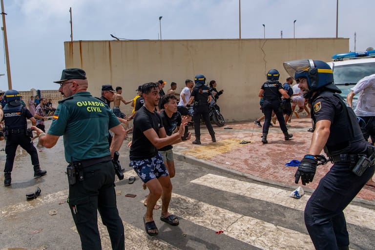 Spanish police officers respond as migrants cross from Morocco into the Spanish enclave of Ceuta, Thursday, July 30, 2026. (AP Photo/Antonio Sempere)