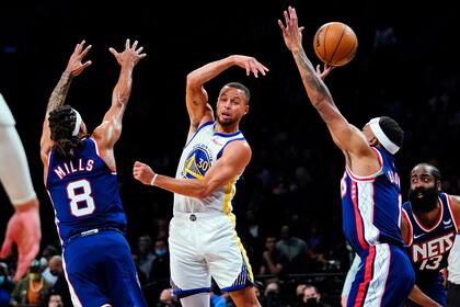 Stephen Curry (30), de los Warriors de Golden State, pasa ante la marca de Patty Mills (8) y Bruce Brown (1), de los Nets de Brooklyn, durante la primera mitad del juego de la NBA, el martes 16 de noviembre de 2021, en Nueva York. (AP Foto/Frank Franklin II)