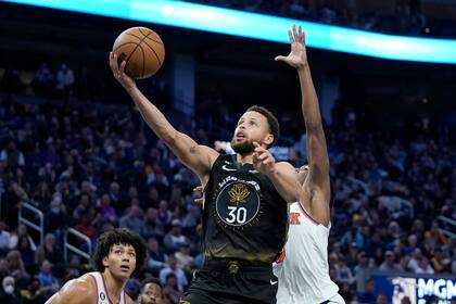 Stephen Curry de los Warriors de Golden State lanza ante el base de los Knicks de Nueva York, Immanuel Quickley, durante la segunda parte del juego de la NBA, el viernes 18 de noviembre de 2022, en San Francisco. (AP Foto/Jeff Chiu)
