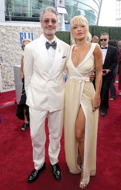 Taika Waititi y Rita Ora se destacaron por su estilo moderno: el director con smoking blanco y la cantante con un escotado vestido de
Miu Miu, anudado a la cintura, desde donde partía una falda envolvente con abertura frontal. Completó su look con joyas de Hearts on Fire