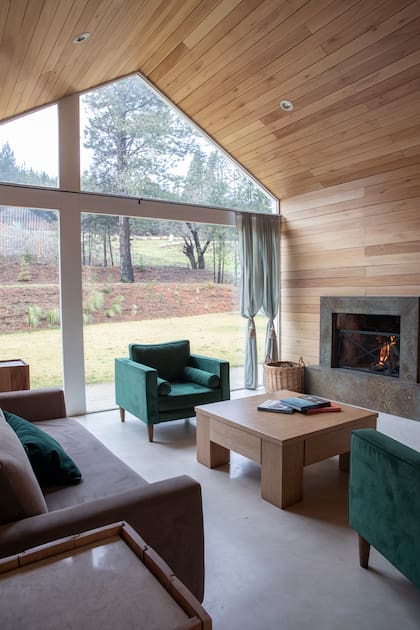 Techo y paredes revestidas en madera de eucalipto. El hogar es una única pieza de piedra natural oxidada (Arq. Tulio Rossini). Sillones tapizados en pana lavable verde.