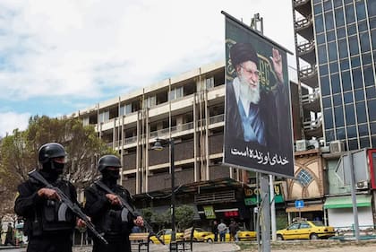 Miembros de las fuerzas de seguridad iraníes hacen guardia en una calle junto a una valla publicitaria del líder supremo de Irán, el ayatolá Alí Jamenei, fallecido en los primeros ataques del sábado.