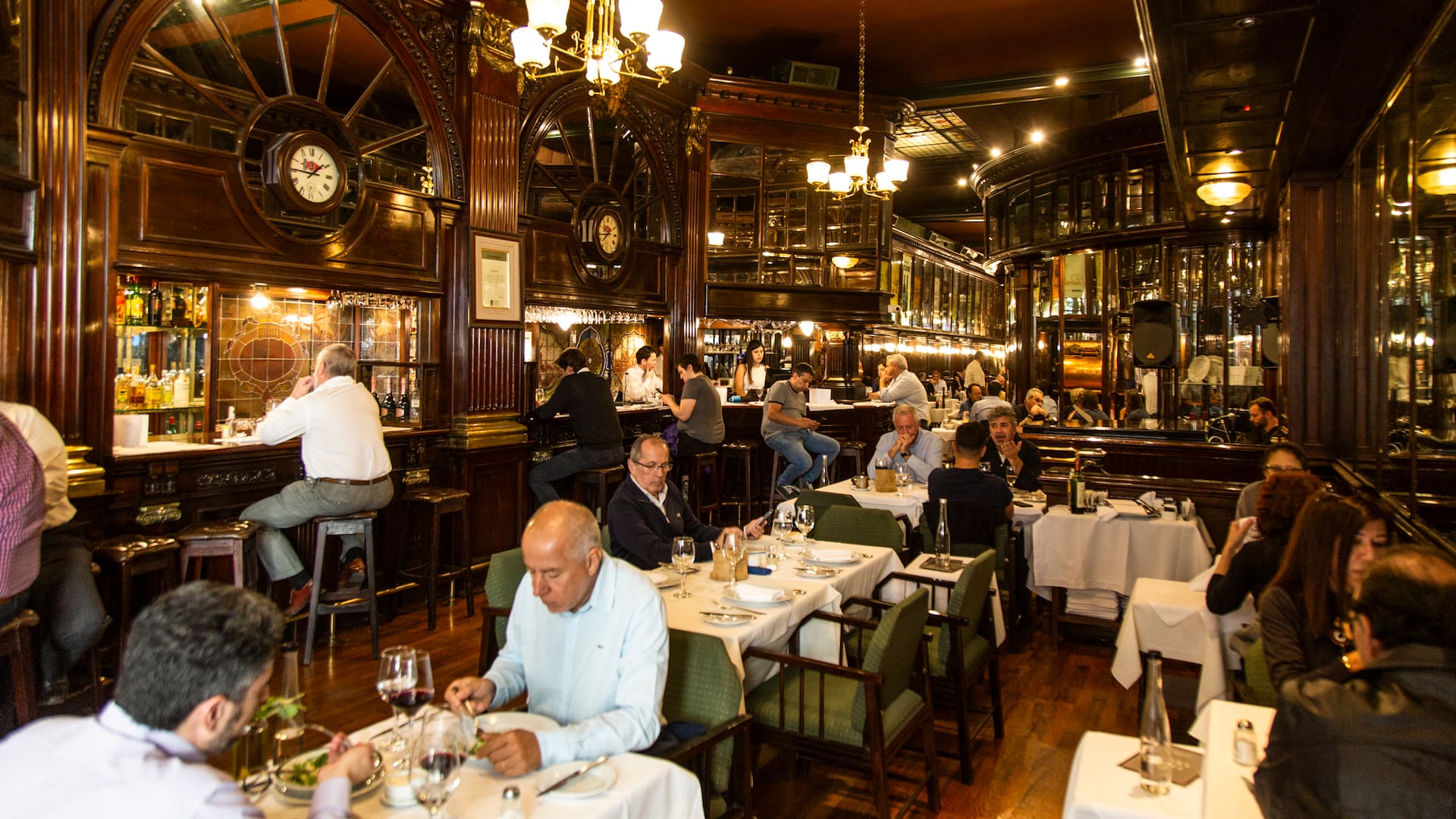 The New Brighton impacta con la barra de madera rojiza y los taburetes donde sentarse a beber un Negroni, la boiserie de cedro en las paredes, el pulido del parqué, los espejos y los biselados, los grandes carteles de bodegas tradicionales que recorren el salón, los vitrales de vidrios, el piano imponente