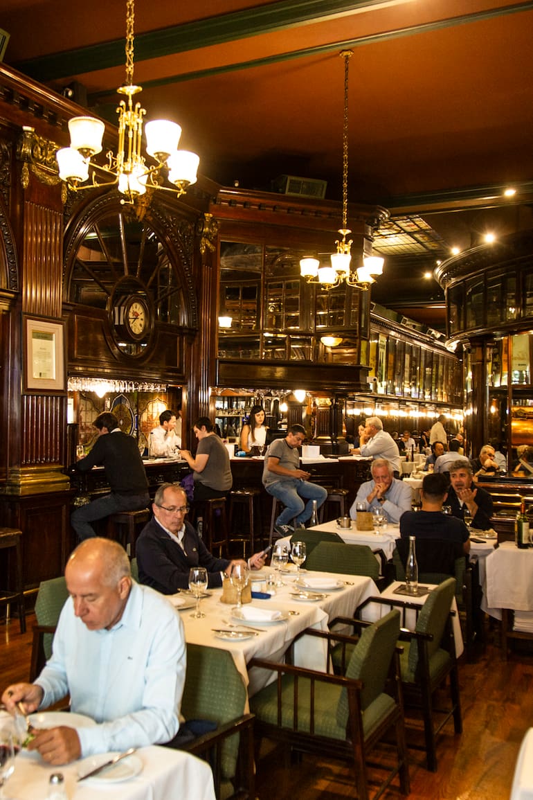 The New Brighton impacta con la barra de madera rojiza y los taburetes donde sentarse a beber un Negroni, la boiserie de cedro en las paredes, el pulido del parqué, los espejos y los biselados, los grandes carteles de bodegas tradicionales que recorren el salón, los vitrales de vidrios, el piano imponente