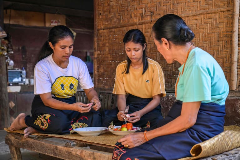 This photo taken on June 24, 2026 Rambu Margaretha (R), a maramba (noblewoman), looking on as two atas (slaves/servants) prepare ingredients for a meal at Kampung Raja Prailiu at Waingapu in East Sumba, East Nusa Tenggara. Two hours from the tourist beaches of Bali, slavery is alive and well on the Indonesian island of Sumba, where people are still being born into bondage. Eight of out 10 of Sumba's population of 685,000 people are Christian but its older "marapu" belief system, that blends animism and ancestor worship, has deep roots. It divides society into three castes, "the nobles, called 'maramba' -- often large landowners -- ordinary people called 'kabihu' and the slaves/servants, the atas," said rights activist Martha Hebi, author of several studies on the subject. (Photo by BAY ISMOYO / AFP) / To go with Indonesia-Sumba-slavery, SPECIAL REPORT by Eric Bernaudeau