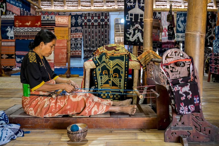 This photo taken on June 24, 2026 shows a woman weaving traditional ikat fabric, a skill passed down among members of the 'ata' (slaves/servants), at Kampung Raja Prailiu at Waingapu in East Sumba, East Nusa Tenggara. Two hours from the tourist beaches of Bali, slavery is alive and well on the Indonesian island of Sumba, where people are still being born into bondage. Eight of out 10 of Sumba's population of 685,000 people are Christian but its older "marapu" belief system, that blends animism and ancestor worship, has deep roots. It divides society into three castes, "the nobles, called 'maramba' -- often large landowners -- ordinary people called 'kabihu' and the slaves/servants, the atas," said rights activist Martha Hebi, author of several studies on the subject. (Photo by BAY ISMOYO / AFP) / To go with Indonesia-Sumba-slavery, SPECIAL REPORT by Eric Bernaudeau
