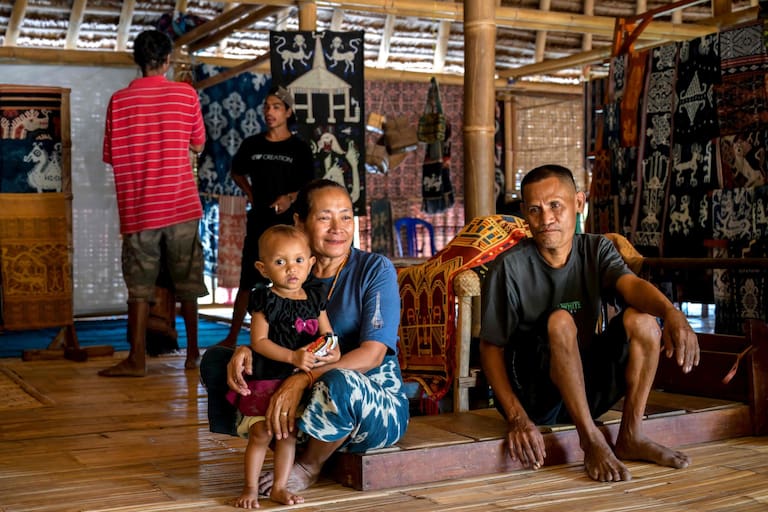 This photo taken on June 25, 2026 shows Tonda Mbitu (C), an 'ata' (slave), sitting with family members alongside their hand-woven fabrics sold as a source of income as they receive no wages from their masters, at Kampung Raja Prailiu at Waingapu in East Sumba, East Nusa Tenggara. Two hours from the tourist beaches of Bali, slavery is alive and well on the Indonesian island of Sumba, where people are still being born into bondage. Eight of out 10 of Sumba's population of 685,000 people are Christian but its older "marapu" belief system, that blends animism and ancestor worship, has deep roots. It divides society into three castes, "the nobles, called 'maramba' -- often large landowners -- ordinary people called 'kabihu' and the slaves/servants, the atas," said rights activist Martha Hebi, author of several studies on the subject. (Photo by BAY ISMOYO / AFP) / To go with Indonesia-Sumba-slavery, SPECIAL REPORT by Eric Bernaudeau