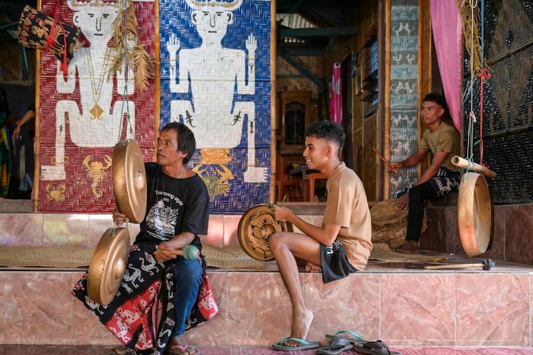This photo taken on June 26, 2026 shows men playing traditional musical instruments during a marapu funeral ceremony for Dicki Takandjandji, a member of the 'maramba' noble class, at Kaburu village at Waingapu in East Sumba, East Nusa Tenggara. Two hours from the tourist beaches of Bali, slavery is alive and well on the Indonesian island of Sumba, where people are still being born into bondage. Eight of out 10 of Sumba's population of 685,000 people are Christian but its older "marapu" belief system, that blends animism and ancestor worship, has deep roots. It divides society into three castes, "the nobles, called 'maramba' -- often large landowners -- ordinary people called 'kabihu' and the slaves/servants, the atas," said rights activist Martha Hebi, author of several studies on the subject. (Photo by BAY ISMOYO / AFP) / To go with Indonesia-Sumba-slavery, SPECIAL REPORT by Eric Bernaudeau