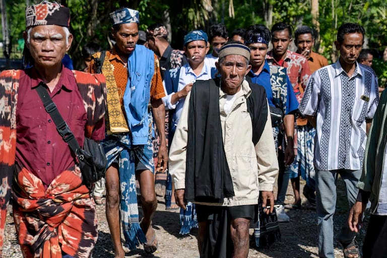 This photo taken on June 26, 2026 shows Sumbanese men, some wearing traditional ikat fabric, attending a marapu funeral ceremony for Dicki Takandjandji, a member of the 'maramba' noble class, at Kaburu village at Waingapu in East Sumba, East Nusa Tenggara. Two hours from the tourist beaches of Bali, slavery is alive and well on the Indonesian island of Sumba, where people are still being born into bondage. Eight of out 10 of Sumba's population of 685,000 people are Christian but its older "marapu" belief system, that blends animism and ancestor worship, has deep roots. It divides society into three castes, "the nobles, called 'maramba' -- often large landowners -- ordinary people called 'kabihu' and the slaves/servants, the atas," said rights activist Martha Hebi, author of several studies on the subject. (Photo by BAY ISMOYO / AFP) / To go with Indonesia-Sumba-slavery, SPECIAL REPORT by Eric Bernaudeau
