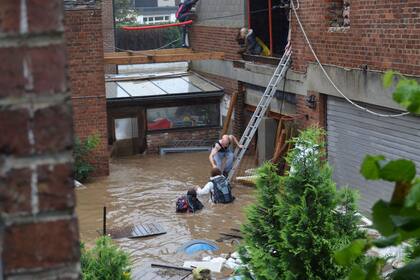 This photograph taken on July 15, 2021 shows a Belgian family being helped to safety after their house was engulfed by floodwaters from the river Vesdre in Trooz. - One month after huge storms battered northwestern Europe and forced an unprecedented wave of floodwater through densely populated valleys, Belgian residents are still in shock. The government of Wallonia has collected 155,000 tonnes of debris but red-brick industrial villages are still cluttered by smashed cars, uprooted trees and furniture ruined by mud and heating oil. (Photo by Charles CLESSENS / AFP)