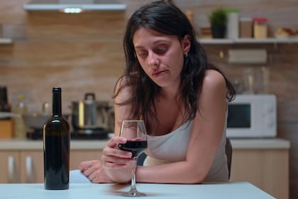 Thoughtful wife looking at a glass of wine sitting on the chair. Unhappy person suffering of migraine, depression, disease and anxiety feeling exhausted with dizziness symptoms having alcoholism