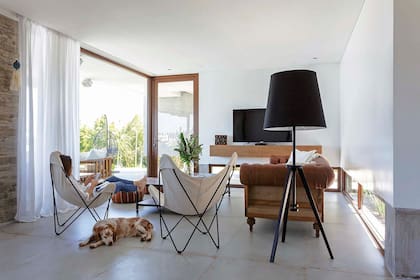 Toda la planta baja tiene piso de porcelanato ‘Garage Toffee’ (SBG). Sillón Chesterfield (Erzebet Restoration) con almohadones y manta (Gloria Atelier Deco). Sillas BKF (Pasto Home Shop) y lámpara de tres patas (La Pantalla).