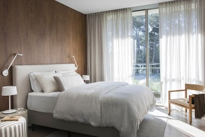 Todos los cuartos comparten una misma paleta neutra que se recorta contra el revestimiento de madera. Lámparas amuradas ‘Demetra Micro Wall’ de la firma italiana Artemide.