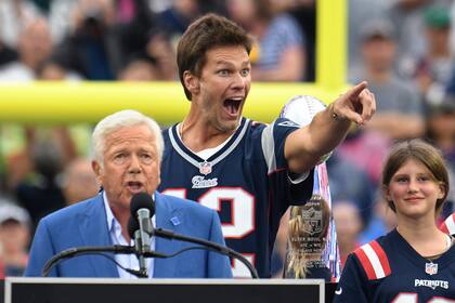 Tom Brady, atrás, quien fuera quarterback de los Patriots de Nueva Inglaterra, señala hacia los fanáticos mientras el dueño del equipo, Robert Kraft, izquierda, habla y la hija de Brady, Vivian, derecha, observa durante la ceremonia de medio tiempo, para honrar a Brady en el partido de la NFL entre los Eagles de Filadelfia y los Patriots, el domingo 10 de septiembre de 2023, en Foxborough, Massachusetts. (AP Foto/Mark Stockwell)