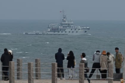 TOPSHOT - A PLA Navy tugboat sails in the Taiwan Strait, past tourists on Pingtan island, the closest point to Taiwan, in China's southeast Fujian province on April 7, 2023. (Photo by GREG BAKER / AFP)
