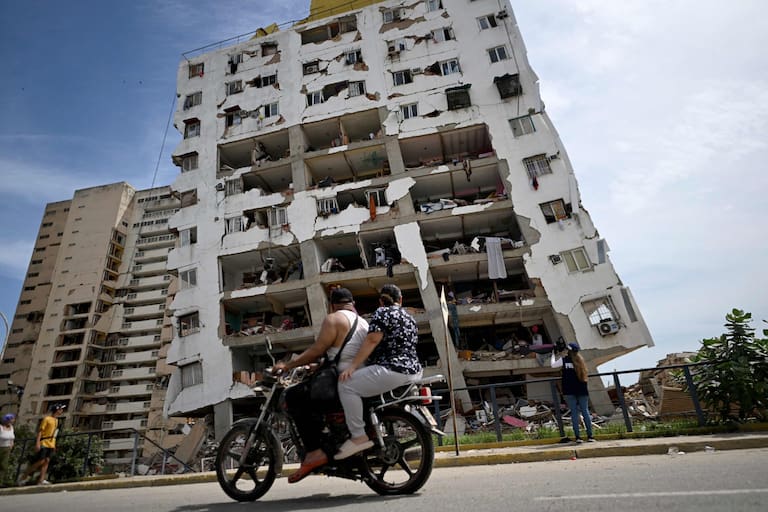 TOPSHOT - Two people ride a motorcycle past a heavily damaged apartment building with its facade torn open following an earthquake in Catia La Mar, La Guaira state, about 30 km northwest of Caracas, on June 25, 2026. A twin earthquake that was Venezuela's largest in over a century has killed at least 164 people and destroyed multiple buildings near the capital, where residents searched on June 25 for missing relatives. (Photo by Juan BARRETO / AFP)