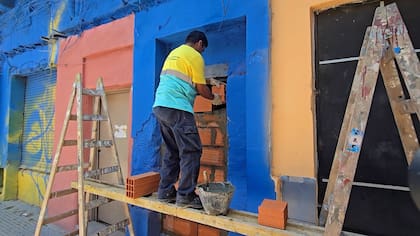 Trabajador coloca ladrillos y cemento para sellar nuevamente la abertura en la fachada azul del inmueble clausurado