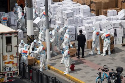 Trabajadores con equipo especial para protegerse del Covid-19 descargan suministros en Shanghái, China. (Chinatopix vía AP)
