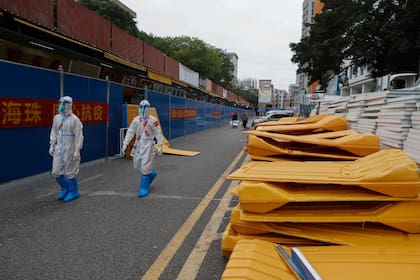 Trabajadores con equipos de protección caminan junto a barricadas desmanteladas a lo largo de una tienda tras la relajación de las autoridades de las restricciones del COVID-19 en el distrito de Haizhu en Guangzhou, en la provincia de Guangdong, en el sur de China, el viernes 2 de diciembre de 2022.