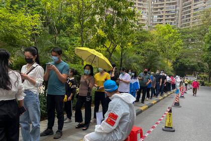 Trabajadores con ropa de protección vigilan a ciudadanos en una fila para hacer pruebas de COVID-19 en un bloque residencial, el lunes 11 de abril de 2022 en Guangzhou, en la provincia sureña china de Guangdong. (Chinatopix Via AP)