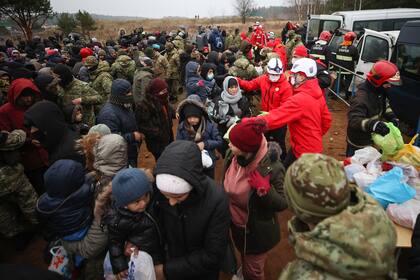 Trabajadores de Cruz Roja bielorrusa entregan ayuda humanitaria a migrantes de Oriente Medio y otros lugares en la frontera con Polonia, cerca de Grodno, Bielorrusia, el martes 16 de noviembre de 2021. (Leonid Shcheglov/BelTA via AP)
