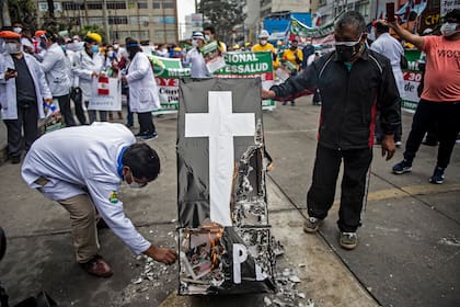 Trabajadores de la salud queman un ataúd simulado mientras protestan frente al Ministerio de Salud peruano exigiendo equipo de protección personal para manejar la nueva pandemia de coronavirus, en Lima, el 29 de septiembre de 2020