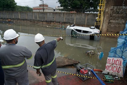 Trabajadores observan un automóvil en el agua y la destrucción causada por las fuertes lluvias durante la noche, en los suburbios de Río de Janeiro, Brasil, el 14 de enero de 2024. (Photo by BRUNO KAIUCA / AFP)