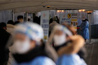 Trabajadores sanitarios, vestidos con equipos de protección, esperan para ayudar a los visitantes de un centro temporal de pruebas de detección del coronavirus, cerca del ayuntamiento de Seúl, en Seúl, Corea del Sur, el 26 de enero de 2022. (AP Foto/Lee Jin-man)