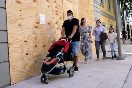 Transeúntes caminan frente a una tienda tapiada en Miami