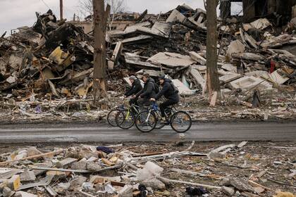 Tres hombres pasan en bicicleta junto a un edificio de apartamentos destruido, en Borodyanka, Ucrania, el 6 de abril de 2022. (AP Foto/Vadim Ghirda)