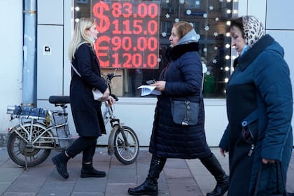 Tres mujeres pasan frente al tablero electrónico de una casa de cambios que muestra la cotización del dólar y el euro en Moscú el 28 de febrero del 2022.