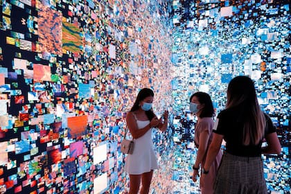 Tres visitantes a la Feria de Arte Digital de Hong Kong junto a una obra inmersiva de Refik Anadol que se convertirá en un certificado digital único (NFT) y se subastará en Sotheby's