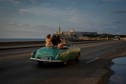 Turistas dan un paseo por el Malecón en un automóvil estadounidense antiguo en La Habana, Cuba, el lunes 16 de mayo de 2022. El gobierno de Joe Biden anunció que ampliará los vuelos a Cuba y levantará las restricciones de la era de Donald Trump sobre las remesas que los inmigrantes pueden enviar a la isla.  (AP Foto/Ramón Espinosa)