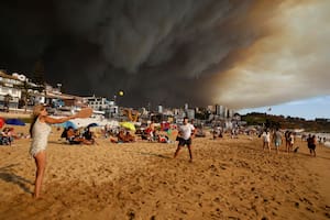 Turistas juegan a las palas en una playa con una gran nube de humo negro a sus espaldas, procedente de los incendios forestales, en Viña del Mar, Chile, el viernes 2 de febrero de 2024. (Martín Thomas, Aton Chile vía AP)