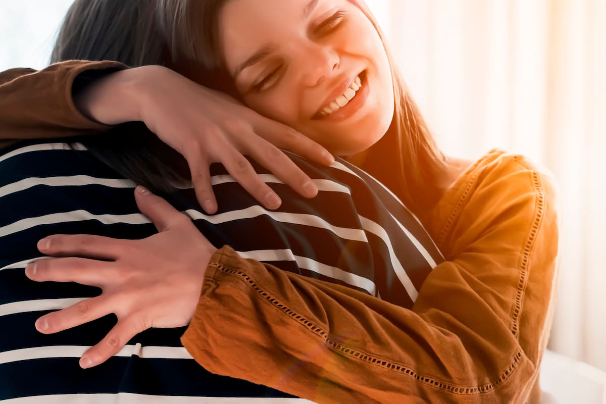 Two friends are embracing in the sun and happy to meet each other. Girls celebrate the holidays or anniversary and hug tightly and warm, feel an emotional connection and love, smiley face closeup.