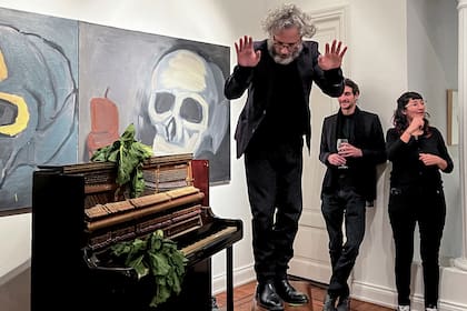 Ulises Conti junto al piano, el atado de acelga y la enorme pintura de Luis Frangella, en la galería Cosmocosa