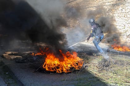 Un agente de la policía retira unas barricadas de neumáticos en llamas colocadas por residentes para evitar que los miembros de pandillas ingresen a su vecindario de Puerto Príncipe, Haití, el martes 19 de noviembre de 2024. (AP Foto/Odelyn Joseph)