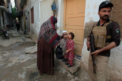 Un agente de policía monta guardia mientras una trabajadora de salud, en el centro, administra una vacuna contra la polio a una niña en un vecindario de Peshawar, Pakistán, el lunes 28 de octubre de 2024. (AP Foto/Mohammad Sajjad)