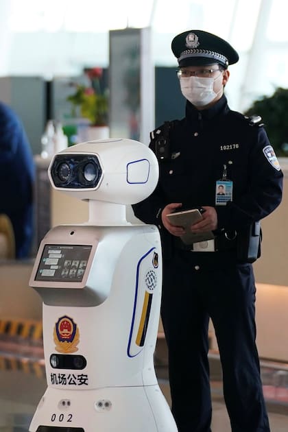 Un agente de segurida junto a un robot policía en el aeropuerto de Wuhan.