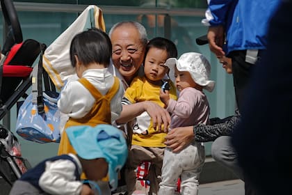 Un anciano juega con niños cerca de un edificio de oficinas en Beijing, el 10 de mayo de 2021. El gobierno chino relajará los límites de natalidad para permitir que todas las parejas puedan tener tres hijos en lugar de dos para hacer frente al rápido envejecimiento de la población, según dijo el lunes 31 de mayo una agencia estatal de noticias. (AP Foto/Andy Wong)