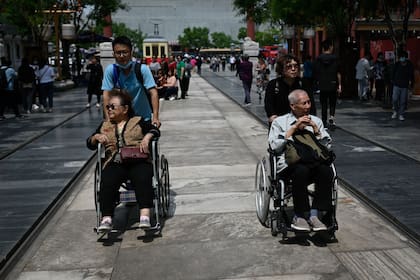 Un anciano y una mujer son empujados en sillas de ruedas a lo largo de una calle en Beijing.