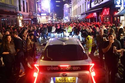 Un automóvil intenta conducir por una calle llena de juerguistas que beben en el área de Soho de Londres