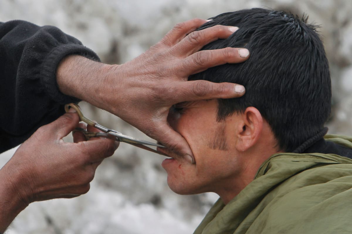 Un barbero callejero afgano, a la izquierda, recorta el bigote de un cliente, con nieve de fondo en Kabul, Afganistán, el 9 de febrero de 2012.