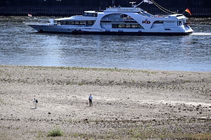 Un barco navega frente a un área seca a orillas del río Rin; se espera que los niveles de agua disminuyan aún más en los próximos días. Federico Gambarini/dpa