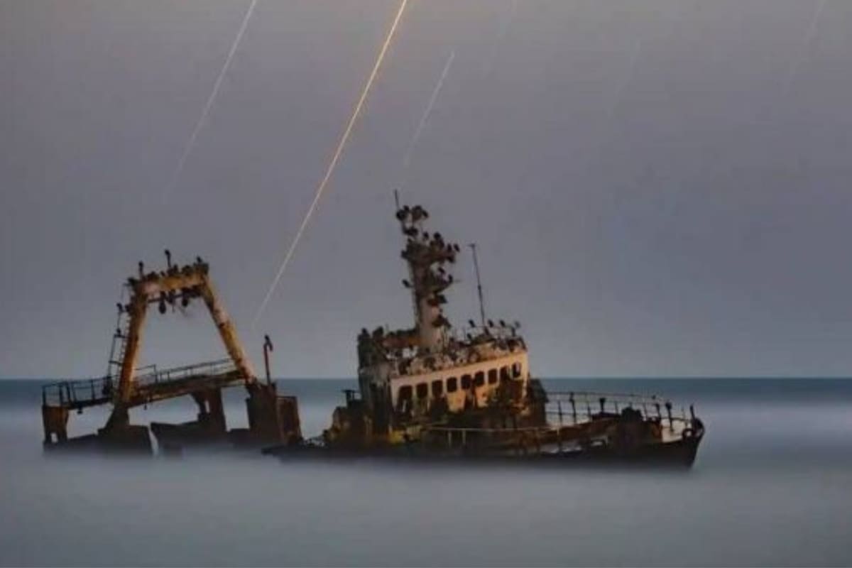 Un barco parece surcar la niebla, iluminado por estelas de estrellas que brillan a través del cielo nublado